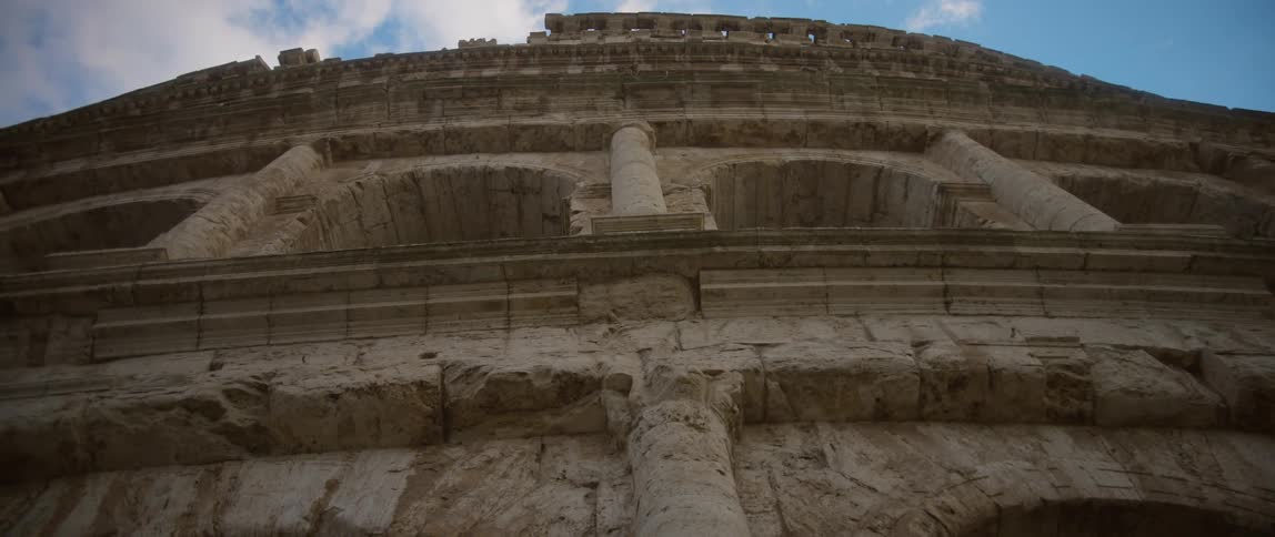 Blue sky and white clouds visible above the facade of the colosseum in rome