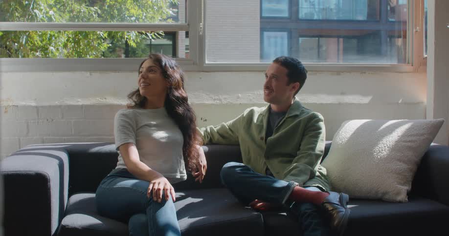 Man and woman sit on couch near open window talking with someone