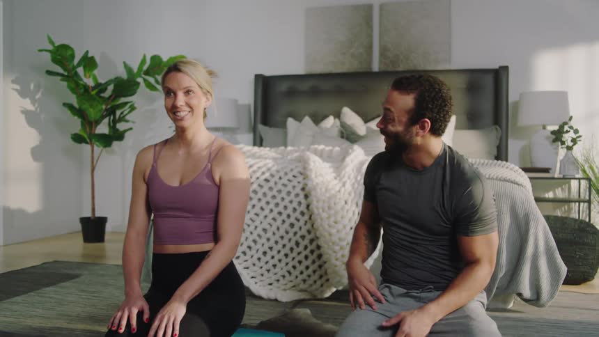 A man laughs as his female companion talks to them while they prepare to exercise at home