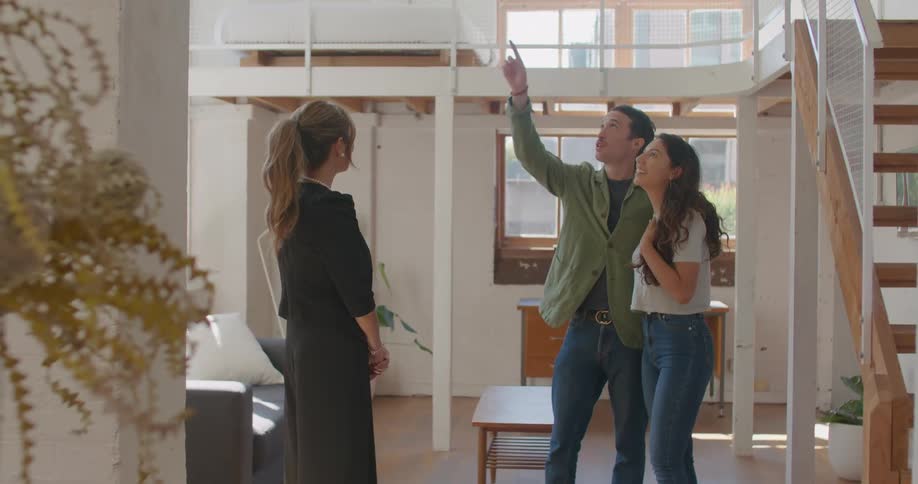 A couple stand in a city apartment with loft and talk with a realtor