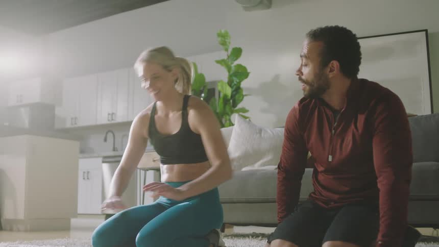A man and a woman perform bodyweight exercises with one another on the floor of a room