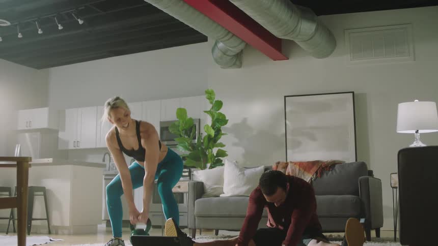 Man and woman workout in living room talking and referencing a tablet