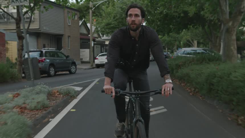 A man rides his bicycle through town past shops and parked cars