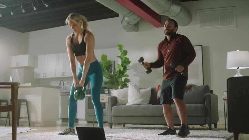 Man and woman are lifting weights together in a house
