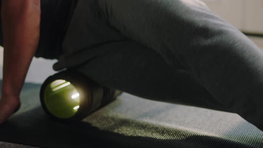 A man rolls out muscles in his leg on a foam roller on a mat
