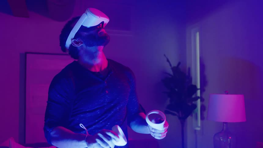 Man wearing a virtual reality headset and holding virtual reality controllers stands in a room and moves his arms around