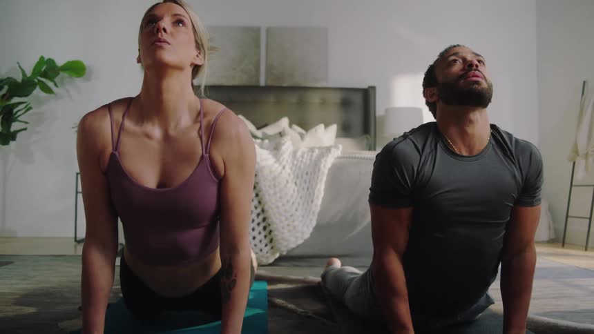 A husband and wife do yoga on mats in their bedroom