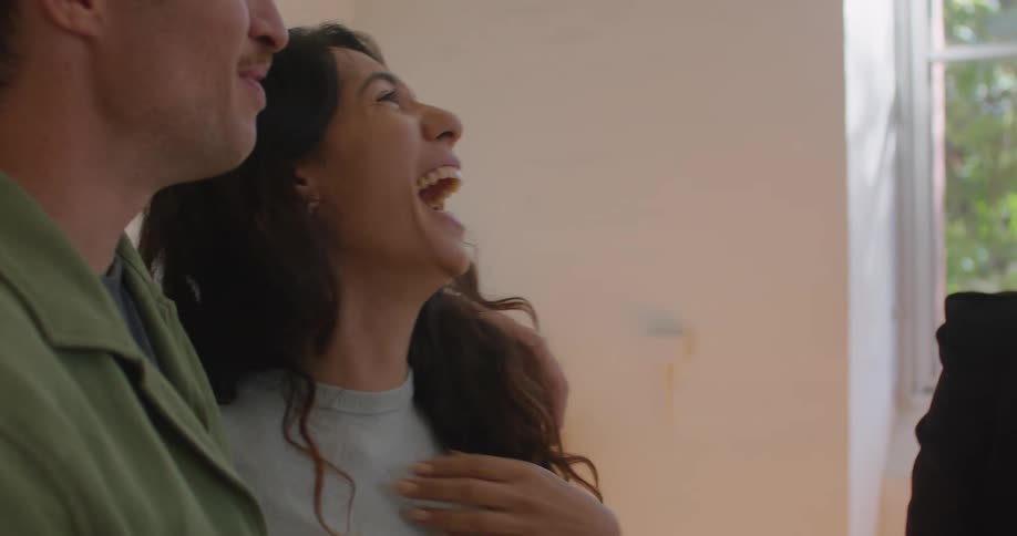 Man with moustache green shirt and woman with gray sweatshirt and wavy hair stands next to real estate agent talking and laughing in room