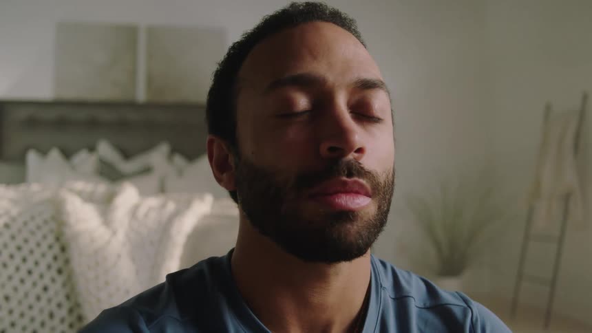 A man is sitting on a floor and deep breathing in a bedroom