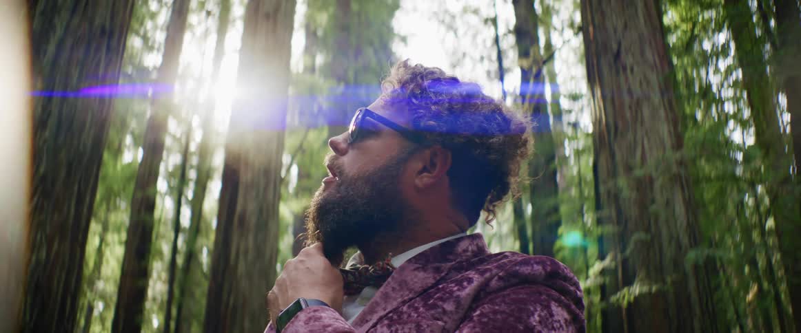 A man is posing for the camera in a wooded area