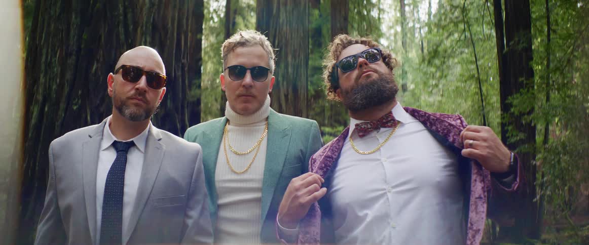 Three men are posing for the camera in a wooded area