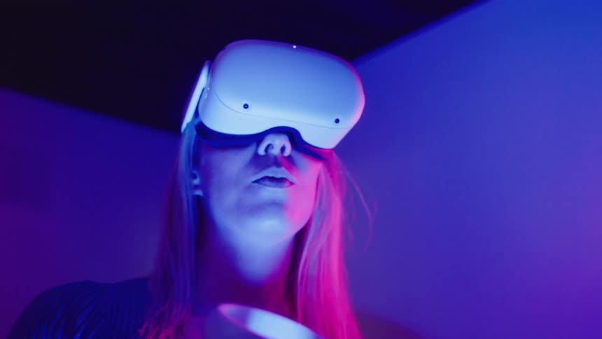 A woman holding hand controllers puts her vr glasses on then looks around and down