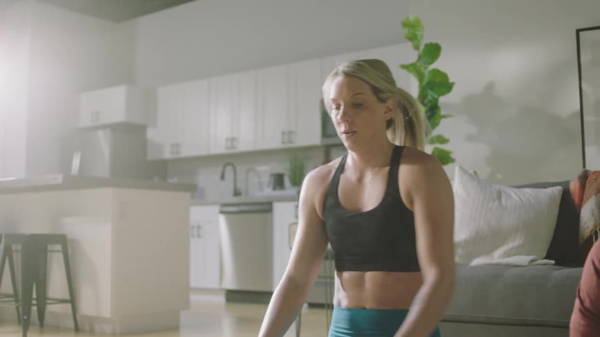 Blonde woman with black sports bra and teal leggings works out next to man with beard and shirt in living room at home