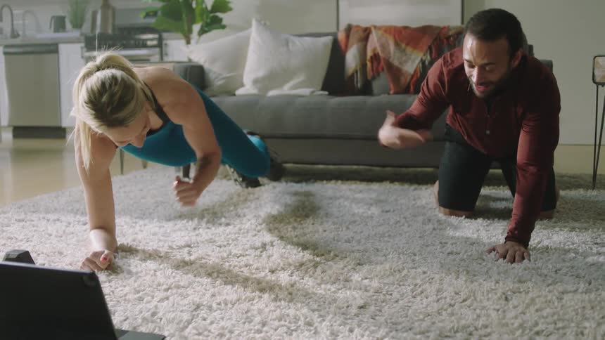 A man and a woman perform exercises on a rug in a room