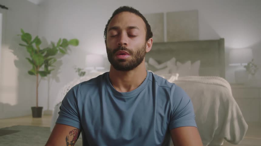 A man is meditating in a bedroom during the daytime
