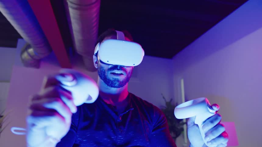 A man is wearing a virtual reality headset and uses controllers in a room