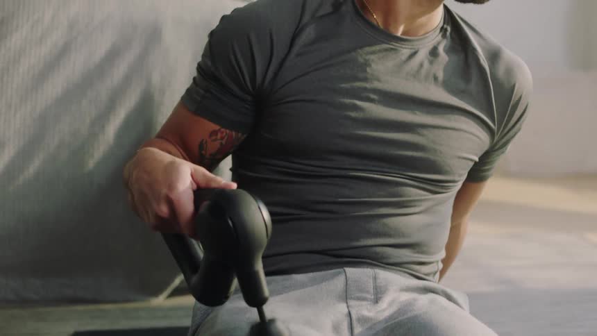 A man using a massager on his thigh muscles while sitting on a yoga mat