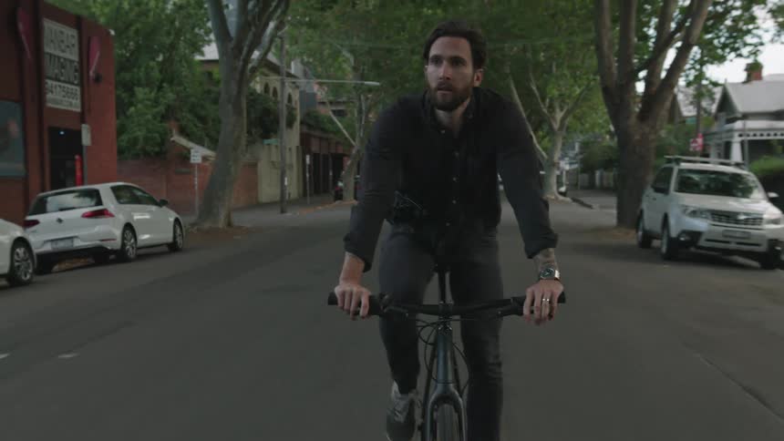 Man cycles along street lined with parked cars in neighborhood