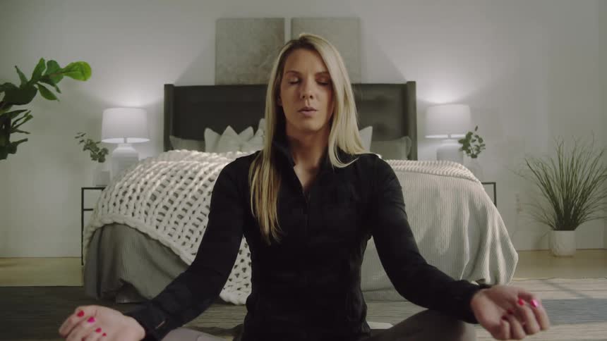 Blonde woman with black shirt does yoga in front of bed in bedroom