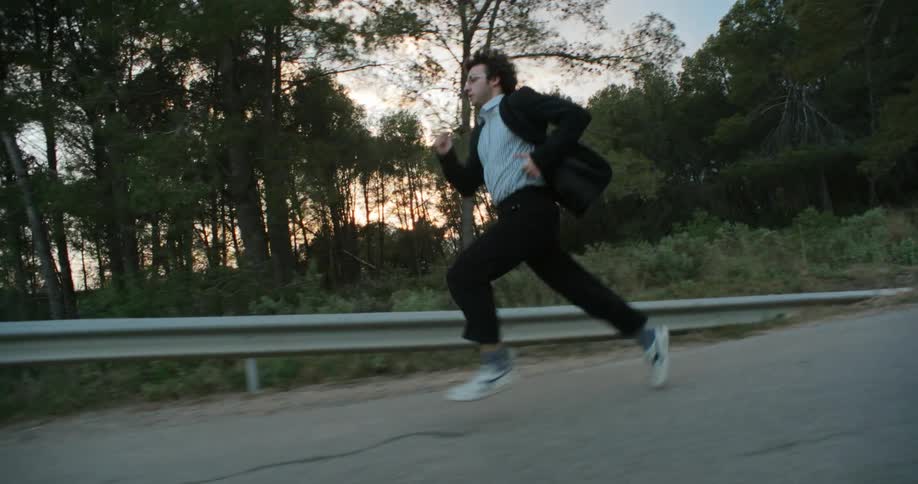 A scared nervous man running on a rural road fleeing away at sunset