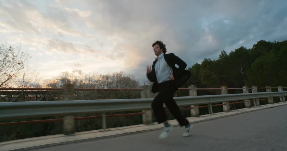 Man wearing semi formal clothes running on a road near the trees at sunset
