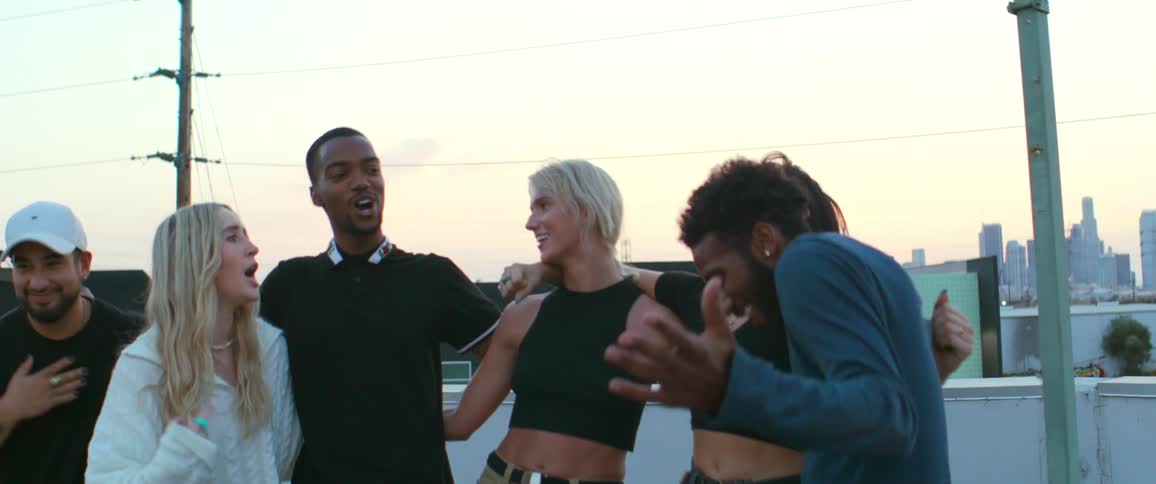 Group of happy young friends dancing and singing together on the roof of a building next to the city skyline