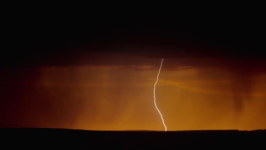 Lightning flashing during a rainstorm over grasslands at sunset