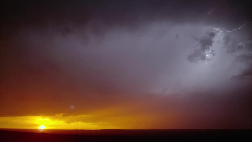 Dark clouds over a red sky as lighting flashes and strikes as the sun is on the horizon