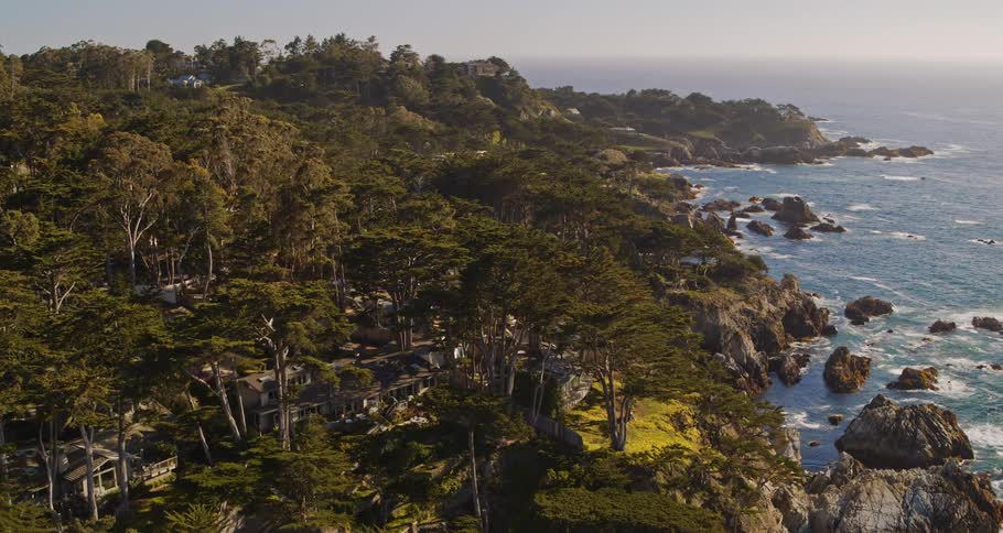 An aerial view of houses on the shore while the waves splash against cliffs