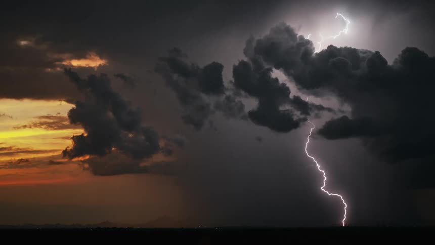 Dark clouds cover an orange sky as lighting flashes and strikes