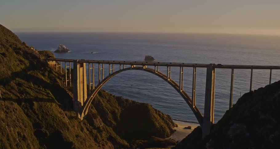 Aerial view of cars driving on a bridge near the ocean at dusk