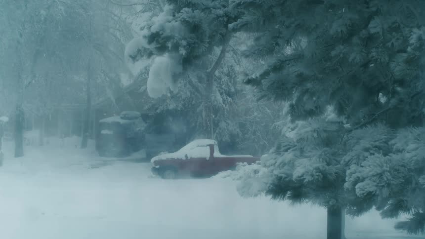 A red truck parked outside during a winter snowstorm