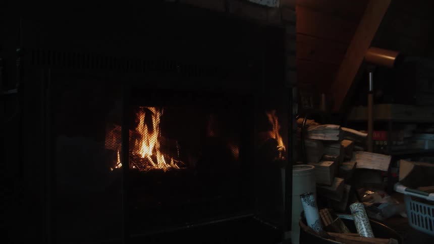 Fire burns in a fireplace behind the protective screen as a lamp and baskets and boxes sit nearby