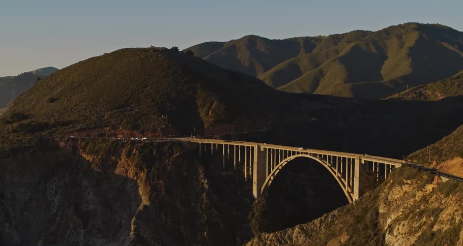 Cars are driving over a bridge near a mountainous area