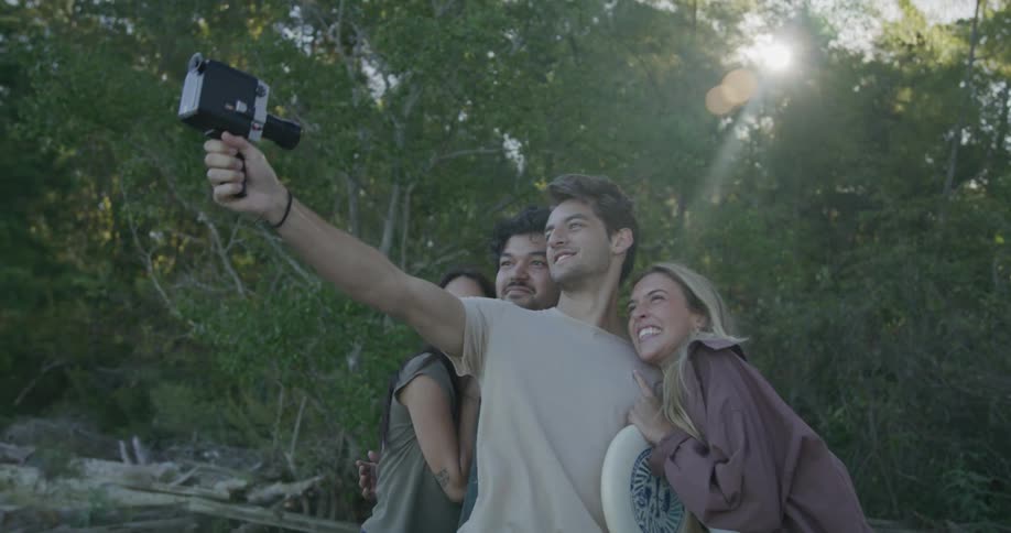 Two couples smile and laugh in the forest as one of the men takes a photo of the group with a video camera