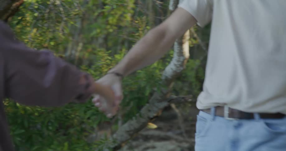 A woman grabs her boyfriends hand as they walk from the woods to the beach
