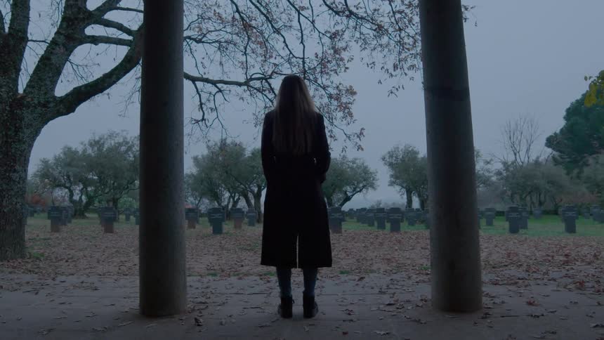A woman standing alone in a graveyard on a chilly autumn day