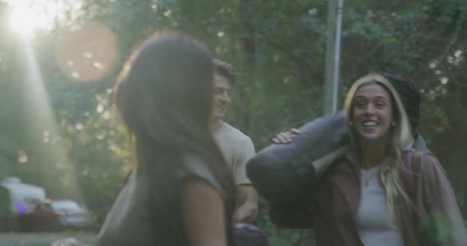 Four teenagers talk and laugh as they carry camping gear from their vehicle