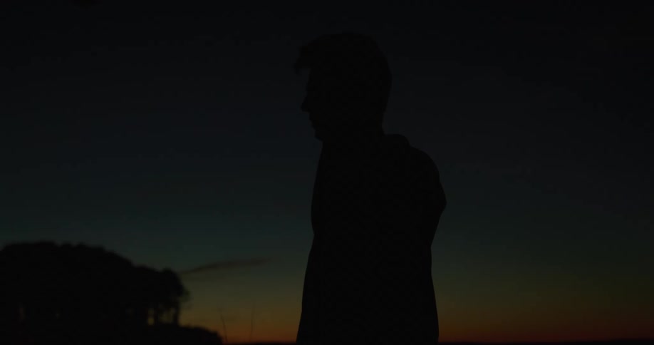 The silhouette of a person making a call on their cell phone outside at night