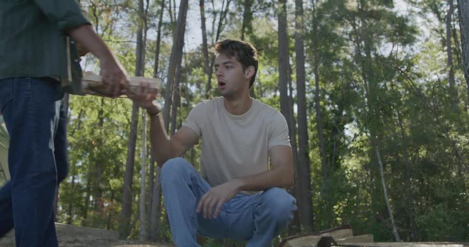 Two men gathering wood and building a campfire in a forest