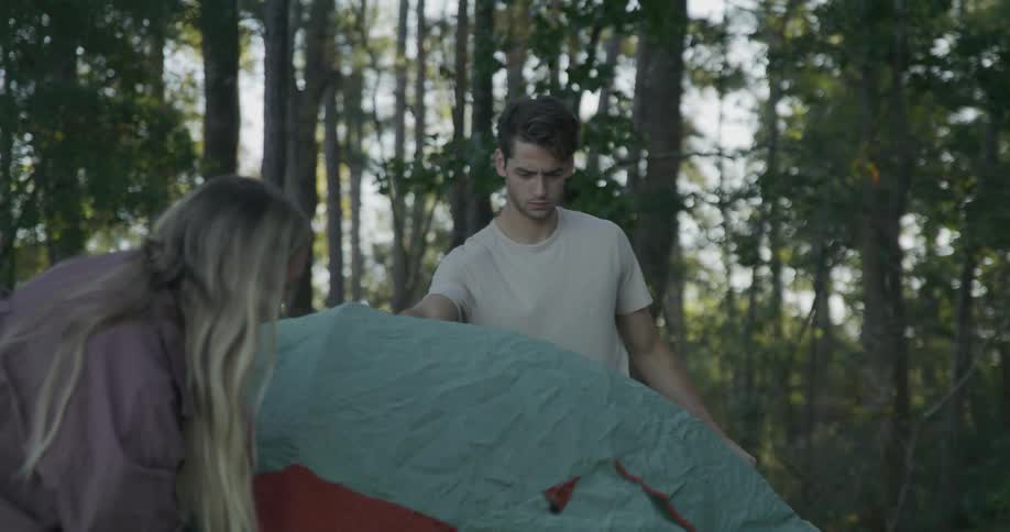 A man and woman setting up a tent in a forest on a summer day