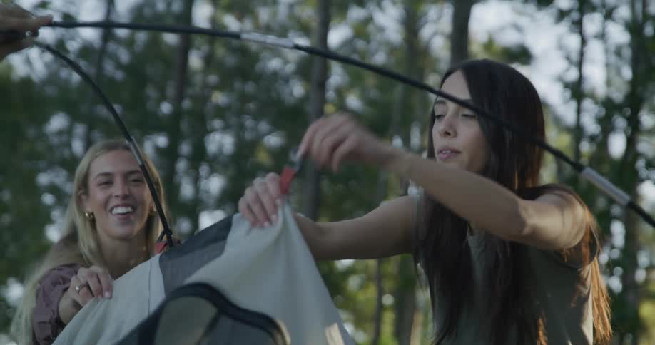 Two teenage girls set a tent up in a forest