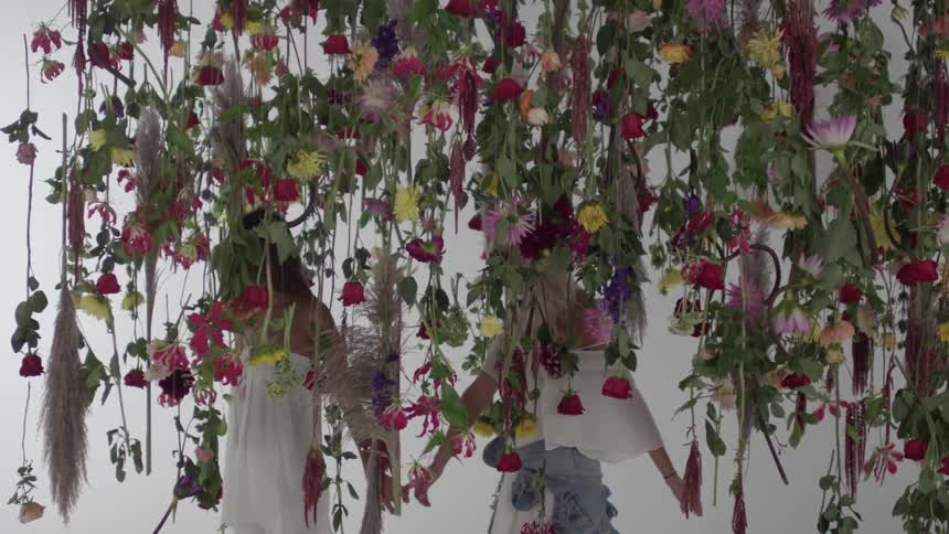 Two women walk through some vines with flowers