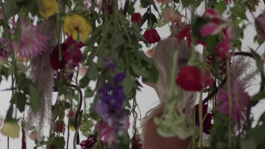 A woman is looking up at some vines covered with flowers