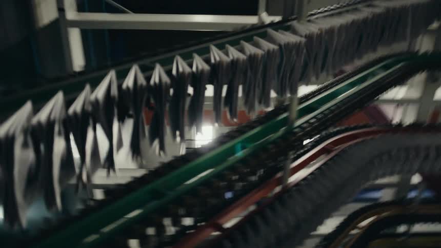 Newspapers are moved along newspaper press machine in large room with fluorescent lights on the ceiling