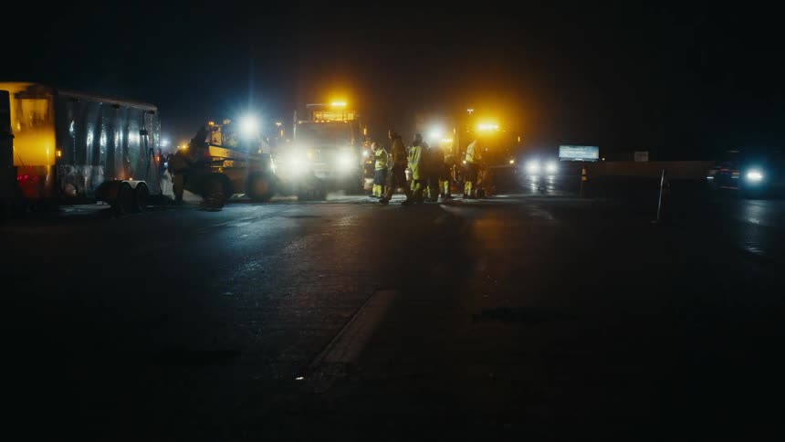 Bright lights flash as construction crews work on a street at night