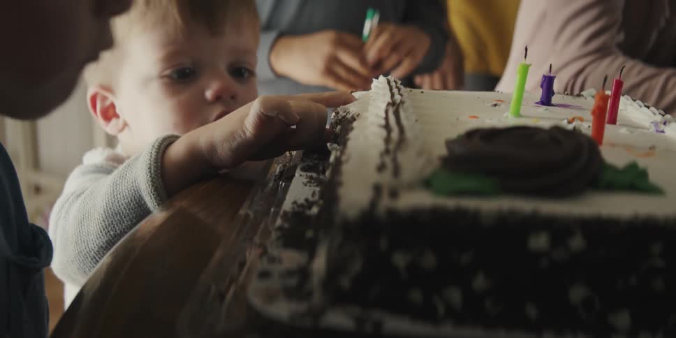 A little boy sticks his finger into the frosting of a birthday cake sneaking a taste