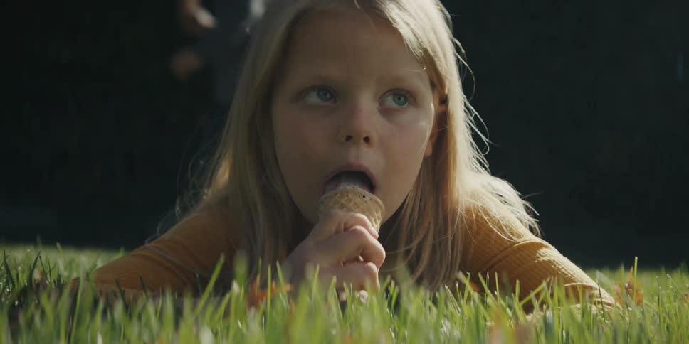 A child laying in grass eating ice cream