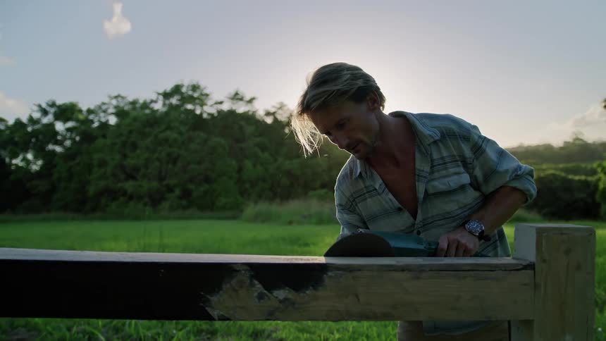 A man is sanding a wooden fence