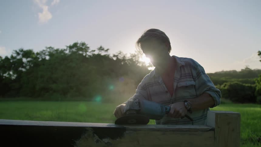 A man is sanding a wooden object in a field